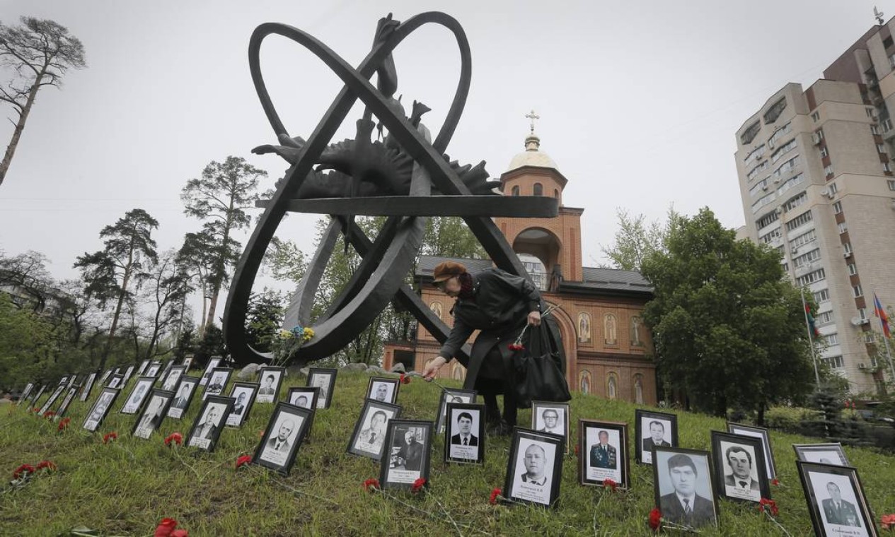 Parente de vítimas da explosão coloca flores ao lado de fotos das 31 vítimas da explosão do reator, em frente ao memorial do desastre em Kiev, capital da Ucrânia. Eram bombeiros, engenheiros e técnicos da usina, que morreram na explosão e ao combater às chamas Foto: Efrem Lukatsky / AP