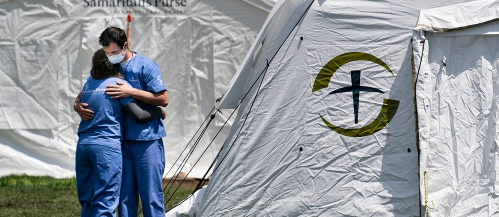 Dois enfermeiros se abraçam em frente a um hospital de campanha montado por um fundo samaritano em Nova York: estado foi um dos que mais sofreu durante a pandemia Foto: ERIN SCHAFF / Agência O Globo