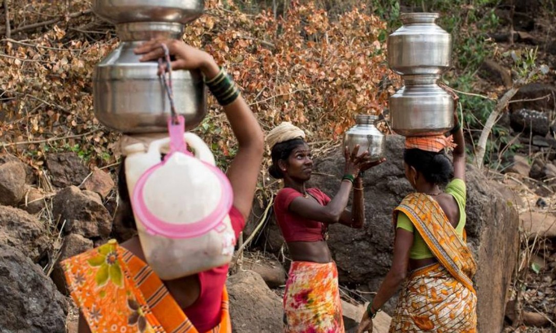 Uma mulher ajuda outra a transportar jarros de metal cheios de água de um poço fora da vila de Denganmal, em Maharashtra, na Índia Foto: Danish Siddiqui / Reuters