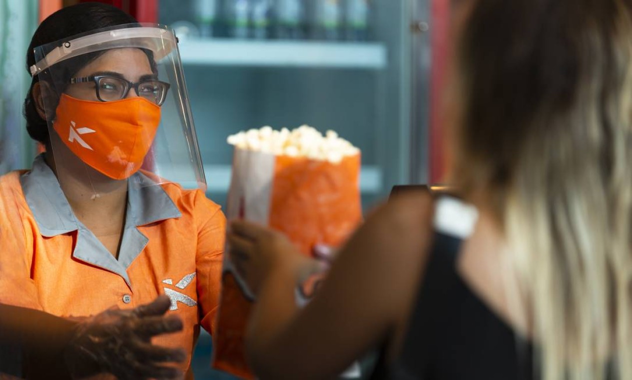 Funcionária usando máscara e escudo facial atende cliente sob novas normas de segurança para funcionamentos dos cinemas Foto: Leo Martins / Agência O Globo