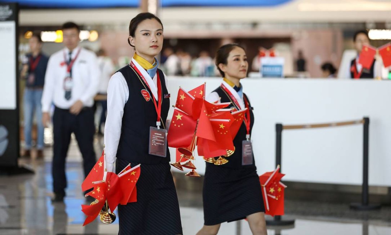 Funcionários passam pelo saguão carregando bandeiras nacionais durante o primeiro dia de operação no novo aeroporto de Pequim Foto: STR / AFP