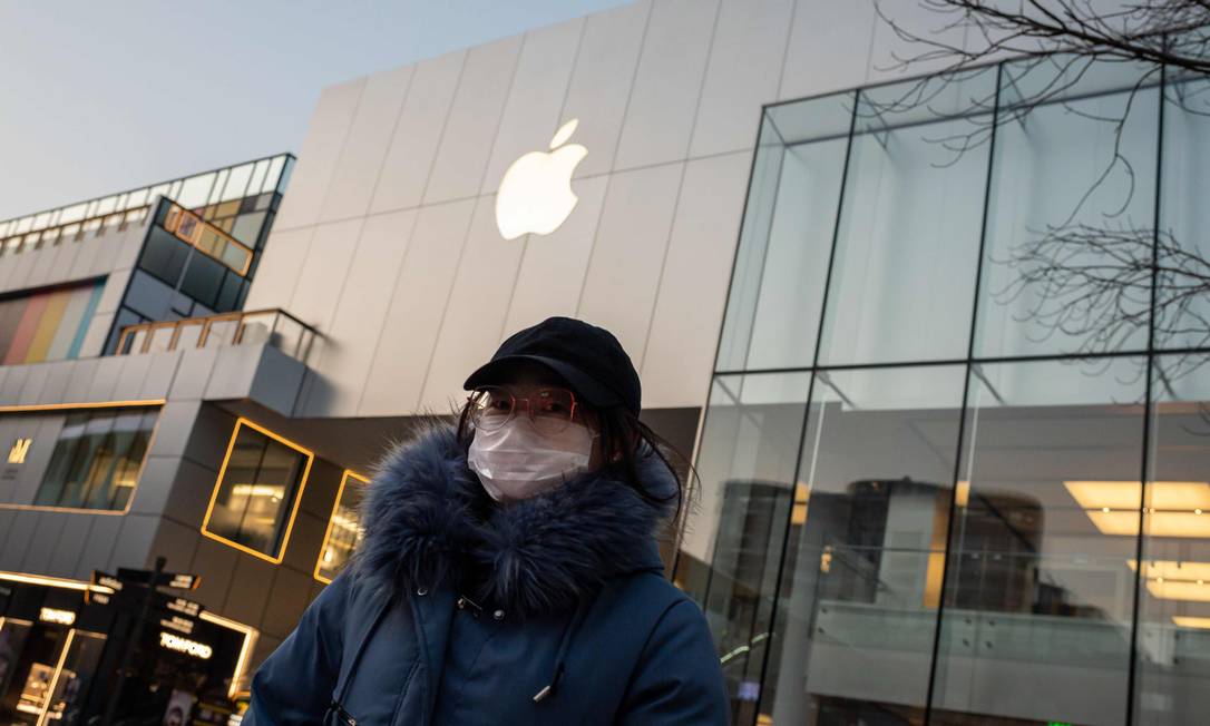 Uma mulher usando uma máscara protetora caminha em frente a uma loja da Apple fechada em Pequim Foto: Nicolas Asfouri / AFP