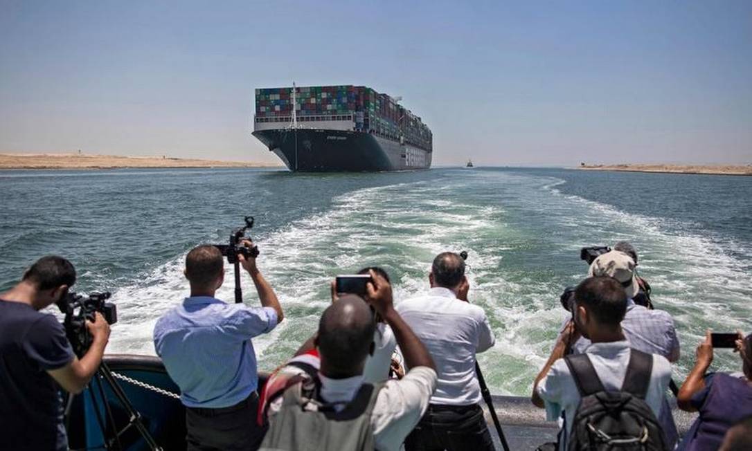 Jornalistas em um barco próximo filmam o porta-contêineres Ever Given, que levantou âncora nesta quarta-feira, depois que foi realizada uma cerimônia para marcar a saída da embarcação do Canal de Suez Foto: AFP