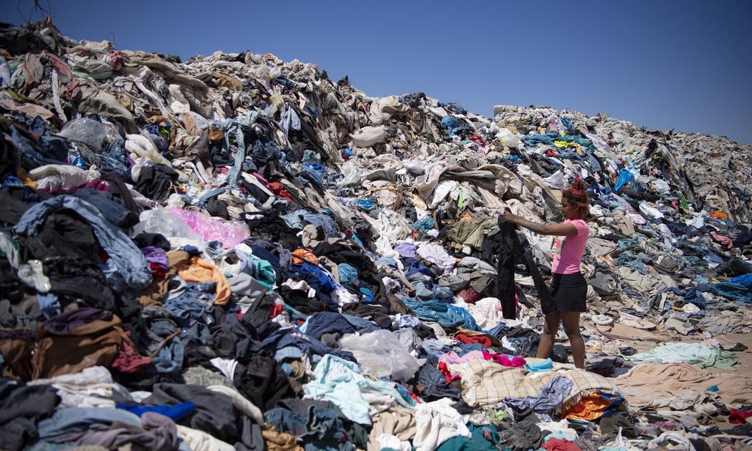 Mulher procura por roupas que lhe sirvam em meio a toneladas descartadas no deserto do Atacama Foto: MARTIN BERNETTI / AFP
