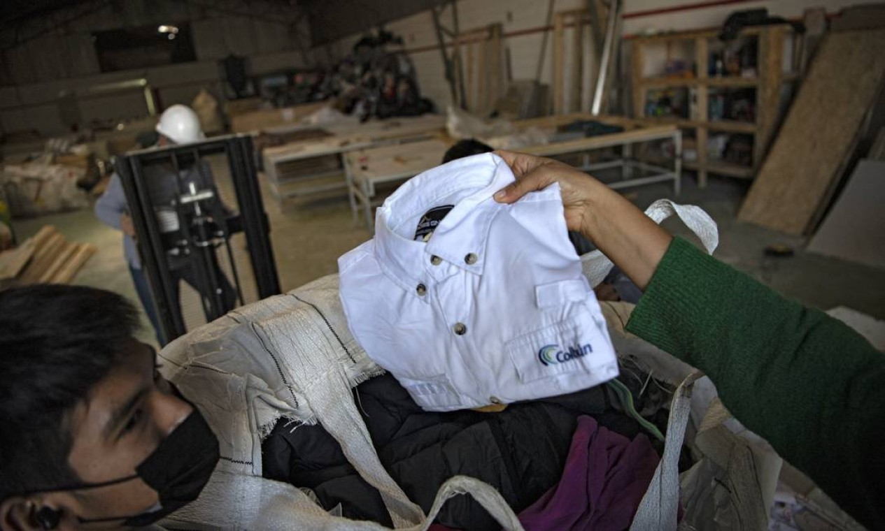 Homens trabalham em uma fábrica que recicla roupas usadas descartadas no deserto do Atacama para painéis de madeira para isolamento de paredes de habitações sociais, em Alto Hospicio, Iquique, Chile Foto: MARTIN BERNETTI / AFP