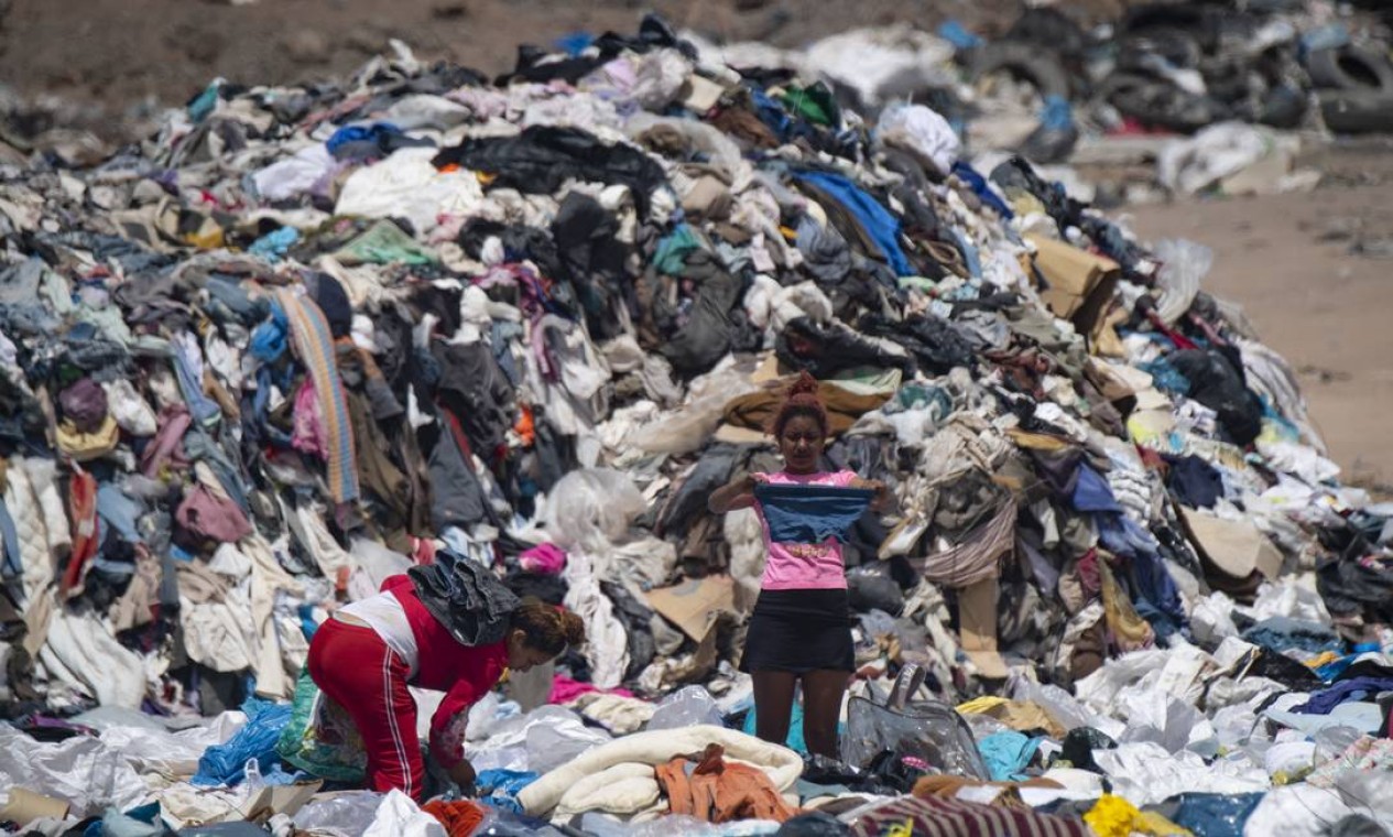 Mulheres buscam roupas em meio a toneladas descartadas no deserto do Atacama Foto: MARTIN BERNETTI / AFP