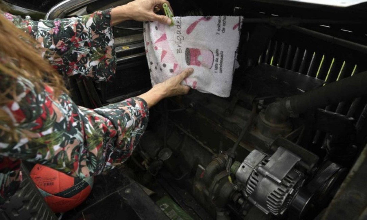 A argentina Candelária Zapp pendura um pano de prato para secar ao lado do motor do carro da família. Foram 22 anos de aventura por vários países, inclusive o Brasil, onde ficaram em confinamento em 2020 por causa da Covid. Foto: Juan Mabromata/AFP