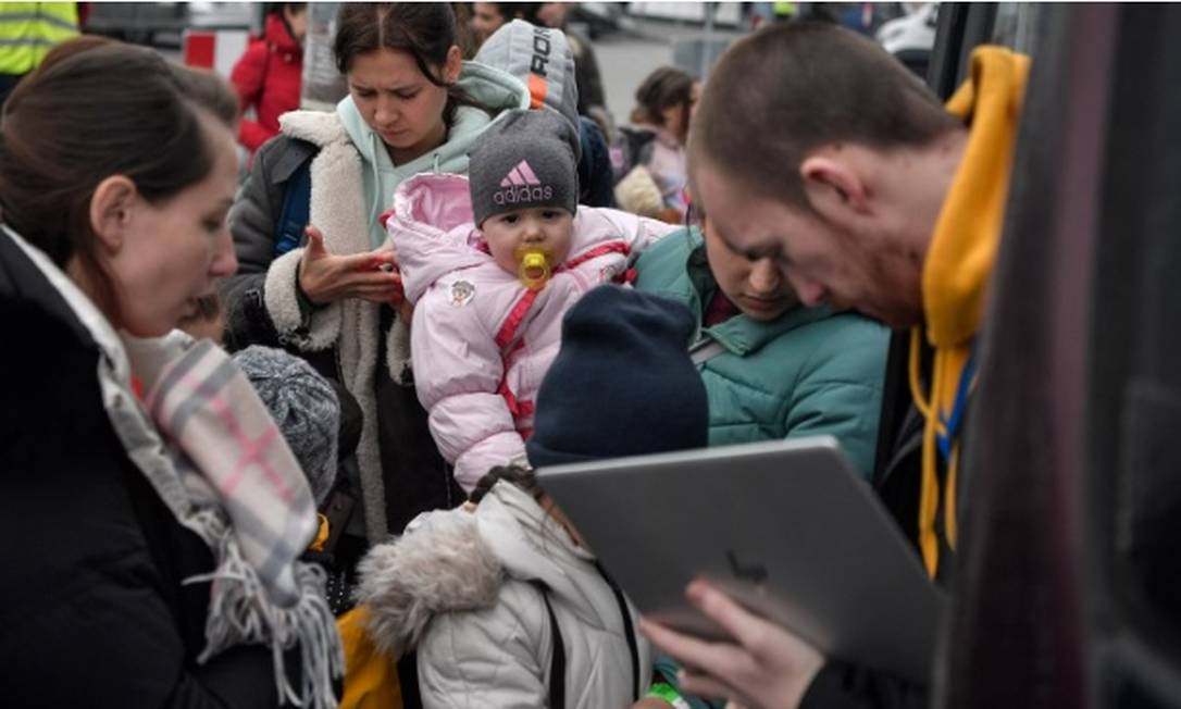 Na Polônia, mulher segura o bebê enquanto homem checa identidades antes do embarque para Portugal Foto: Louisa Gouliamaki/AFP