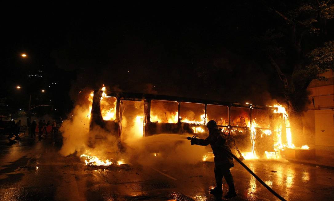 Bombeiro apaga as chamas de ônibus incendiado por vândalos Foto: Pablo Jacob / Agência O Globo