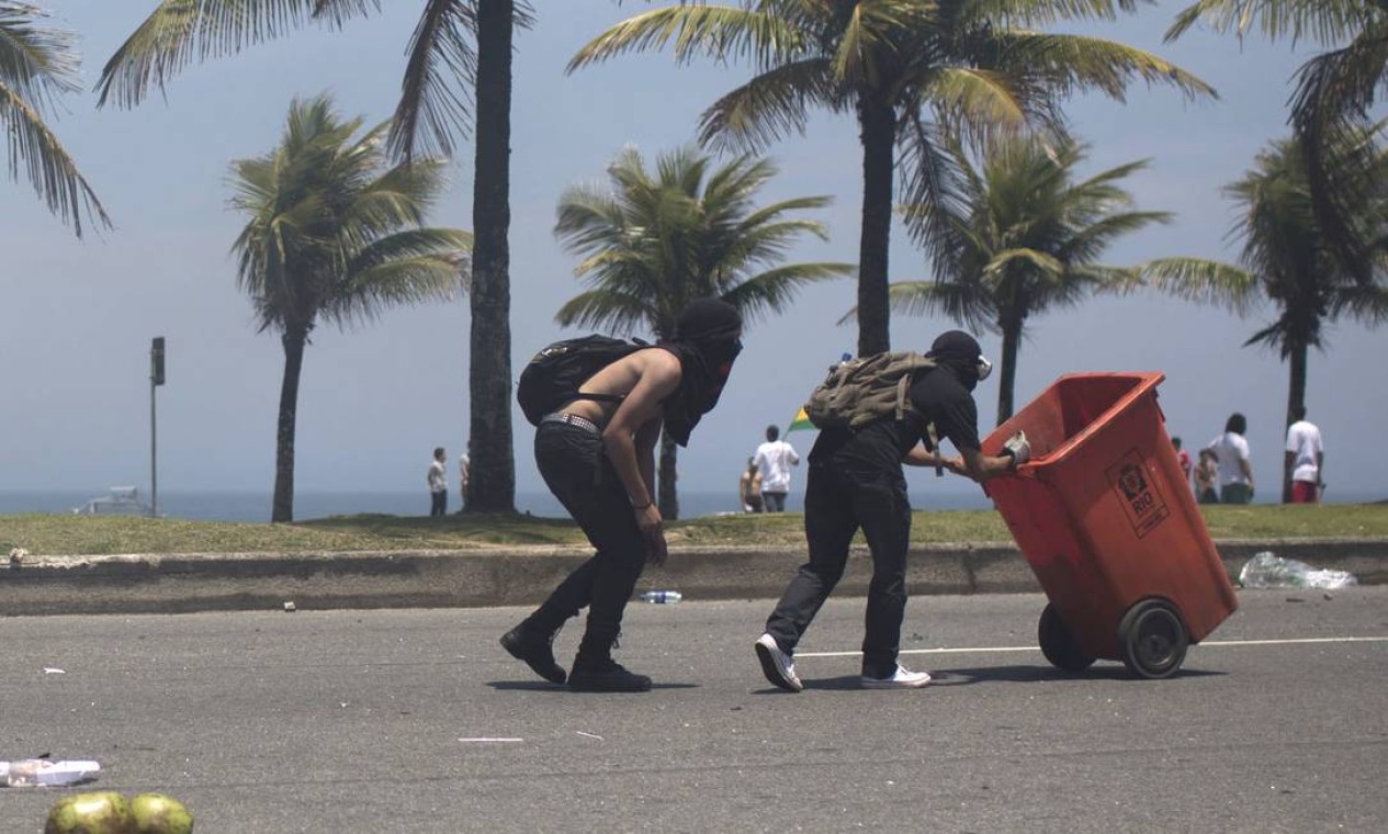 Manifestantes jogam no chão cocos que estavam em latão de lixo da Comlurb e seguem em direção à barreira armada pela Força Nacional na Avenida Sernambetiba Foto: Felipe Dana / AP