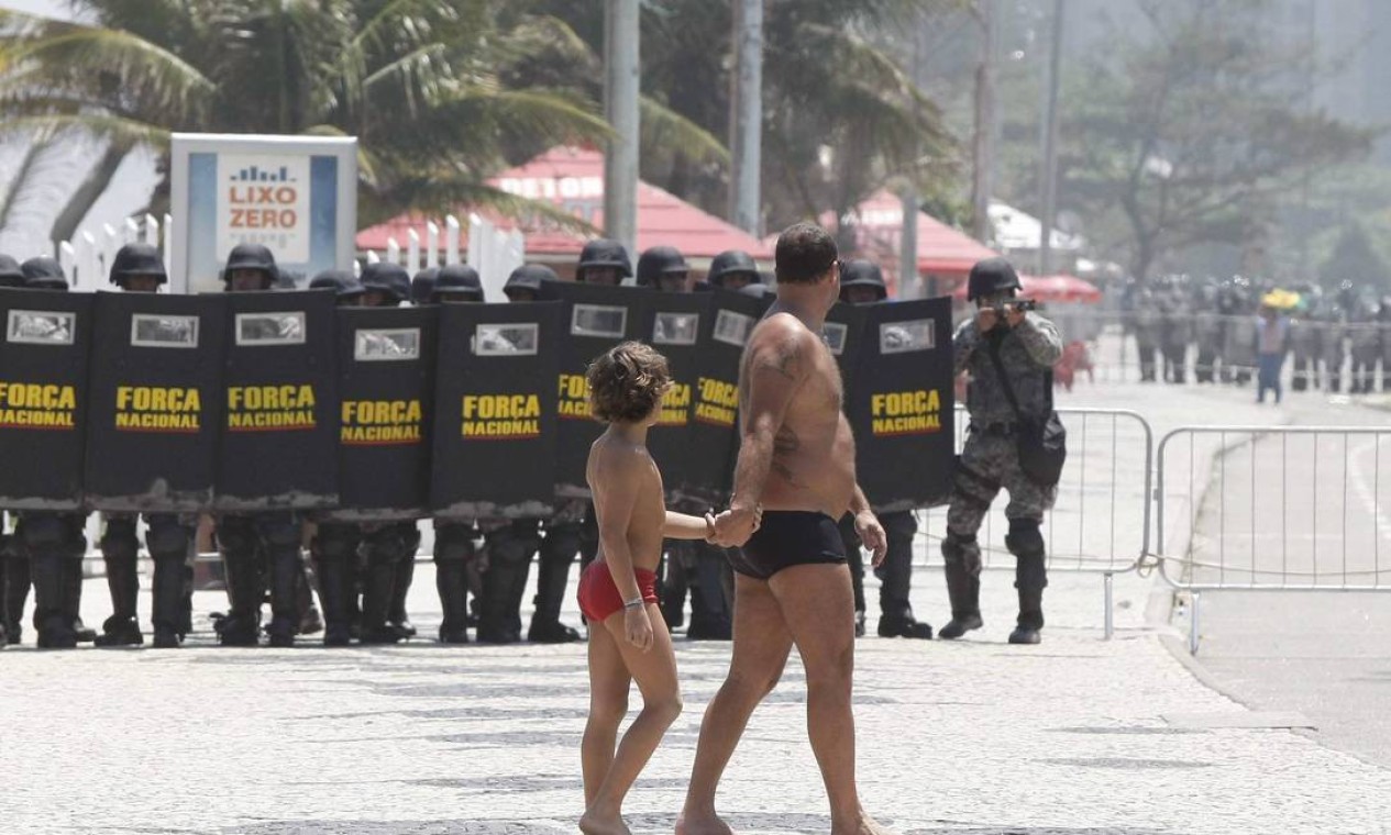 A despeito do confronto entre PMs e manifestantes, um homem e um menino passam de roupa de banho na Avenida Lúcio Costa Foto: Pablo Jacob / Agência O Globo