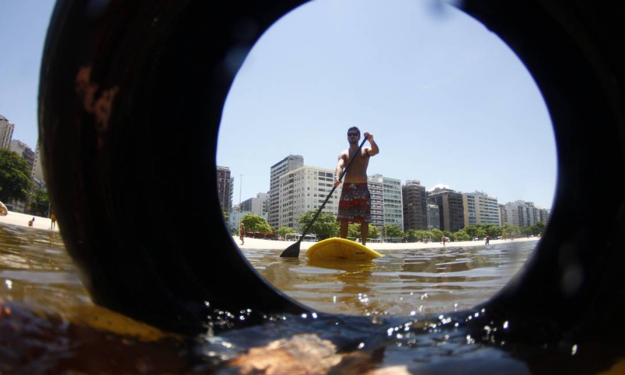No meio do caminho, um pneu: o instrutor de stand up paddle Luiz Rocha na Praia de Icaraí, onde praticantes da atividade às vezes precisam entrar na água "varrendo" o lixo flutuante Foto: Marcelo Piu / Agência O Globo