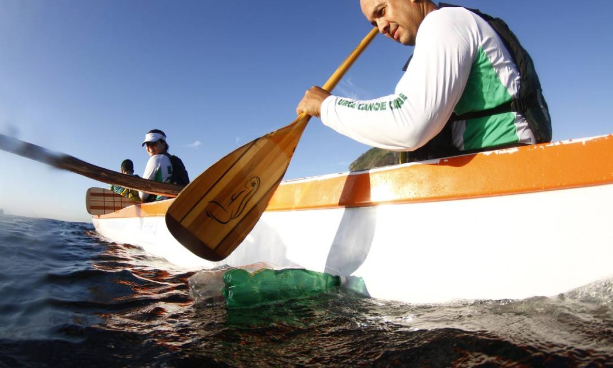 Os adeptos da canoa havaiana também têm a poluição como obstáculo à atividade. Na foto, um remador tenta afastar garrafas pet da rota das embarcações Foto: Marcelo Piu / Agência O Globo