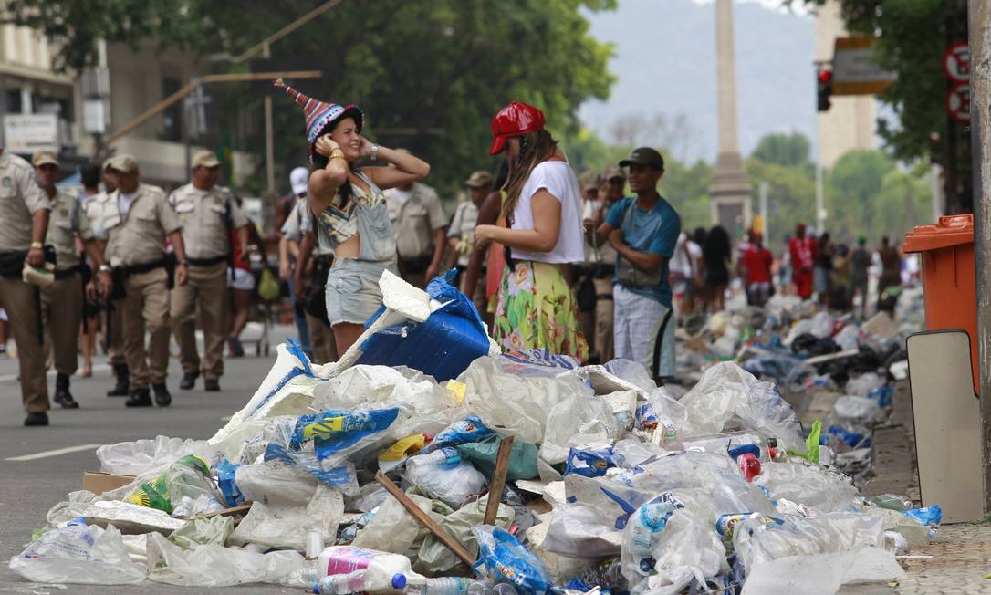 Foliãs caminham em meio ao lixo que toma a Av. Rio Branco Foto: Domingos Peixoto / O Globo