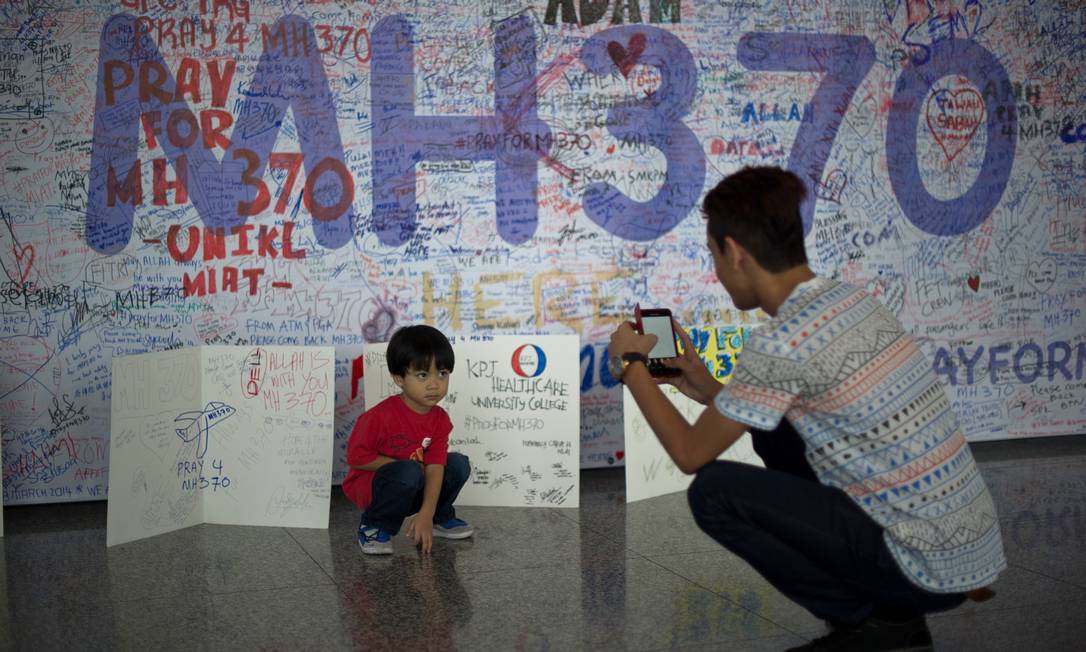 
No aeroporto de Kuala Lumpur, um homem tira fotos de um menino na frente de cartazes com mensagens para os passageiros do avião desaparecido da Malaysia Airlines
Foto: MOHD RASFAN / AFP