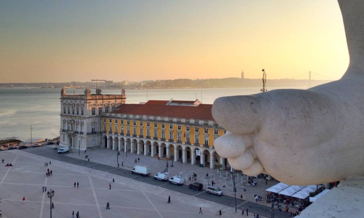 Um dos melhores pontos para ver o pôr do sol em Lisboa é o mirante do Arco da Augusta, no Terreiro do Paço. Visitantes ficam ao lado da estátua no topo do arco Foto: Fernanda Dutra / O Globo