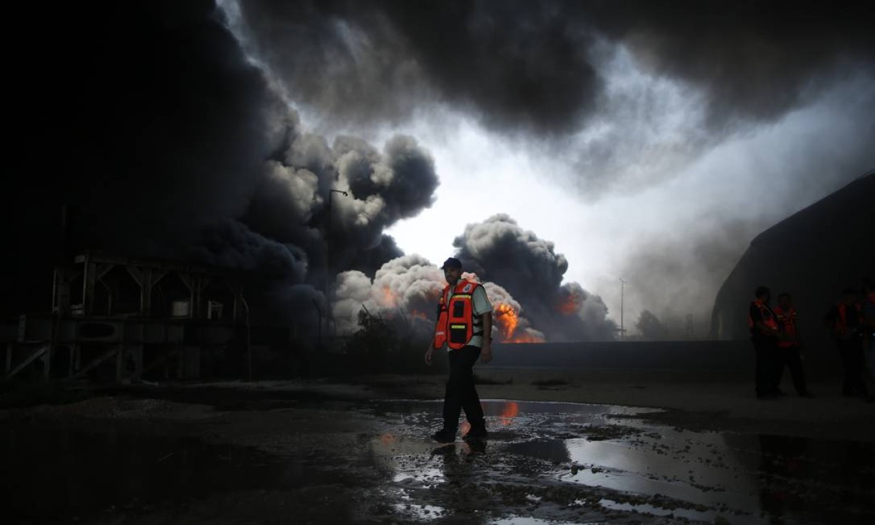Um bombeiro palestino caminha entre as chamas do incêndio. O depósito de combustível do local foi atingindo por bombas, que cortaram a energia da região Foto: MOHAMMED SALEM / REUTERS