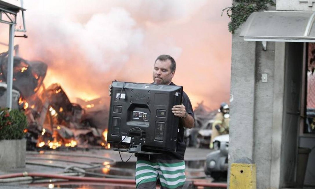 Com o depósito em chamas, homem tenta salvar alguns equipamentos. Funcionários estimam que metade dos carros foi retirada antes do fogo Foto: Urbano Erbiste / Extra