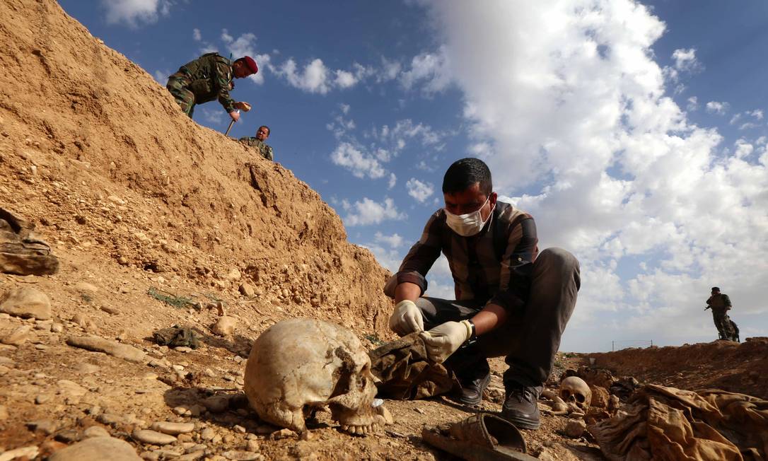 Inspetores iraquianos examinam restos mortais de mebros da minoria yazidi na região de Sinjar. Crianças do grupo estão entre as principais vítimas do Estado Islâmico Foto: SAFIN HAMED / AFP