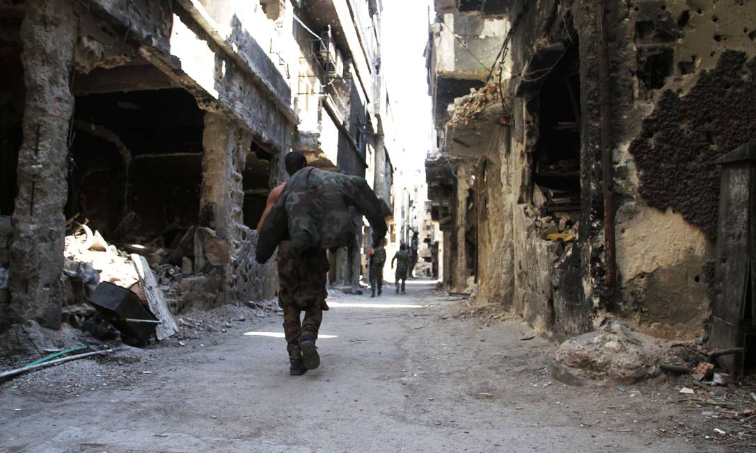 Homem caminha por prédios destruídos no campo de refugiados palestinos Yarmouk, próximo à capital síria, Damasco Foto: YOUSSEF KARWASHAN / AFP