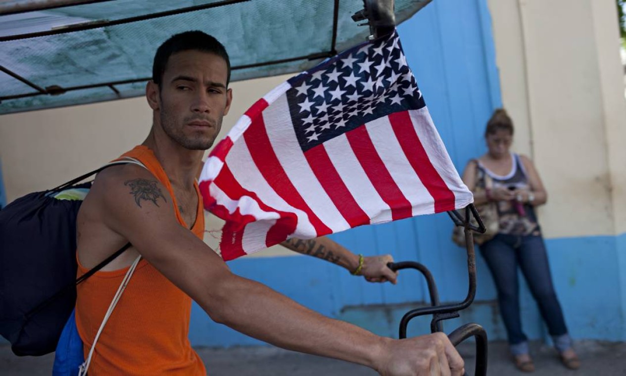 Na bicicleta que usa como táxi, cubano exibe sem receio a bandeira dos EUA Foto: ELIANA APONTE TOBAR / NYT