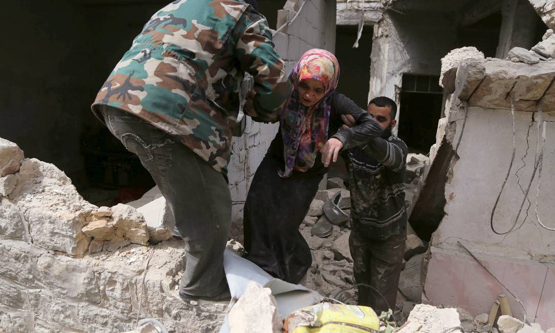Moradores ajudam uma mulher a deixar escombros de sua casa após ataque aéreo realizado por forças leais ao presidente sírio, Bashar al-Assad, em al-Sakhour, um bairro de Aleppo Foto: HOSAM KATAN / REUTERS