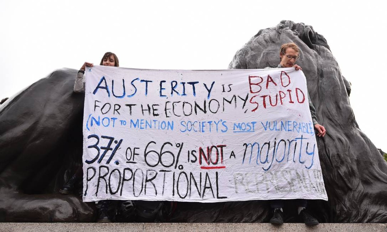 Manifestantes sobem em um dos leões de Trafalgar Square para exibir uma faixa contra medidas de austeridade Foto: BEN STANSALL / AFP