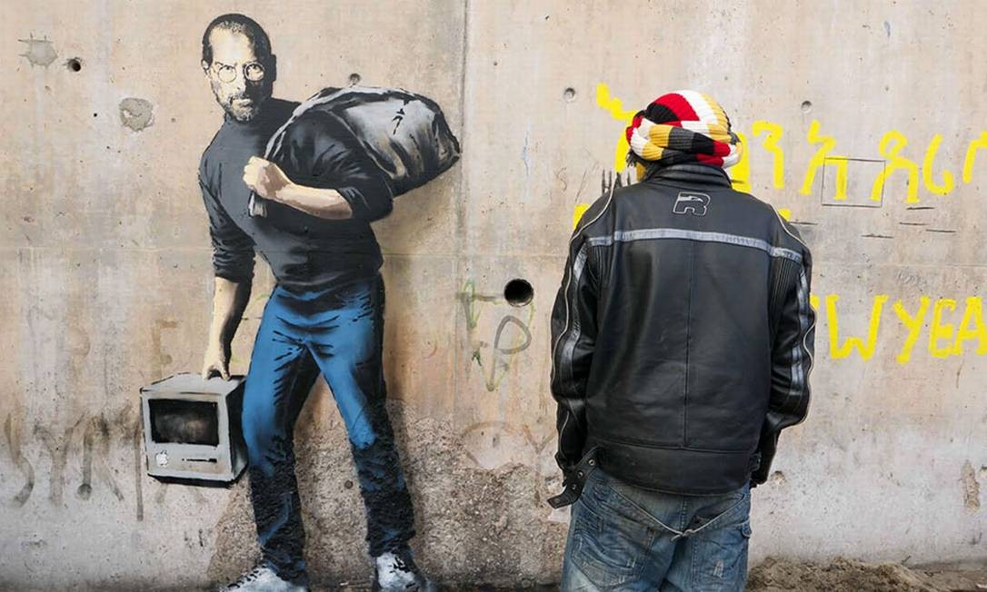 No grafite &#039;Filho de um imigrante da Síria&#039;, localizado em Calais, onde está situado um campo de refugiados, o artista lembra que o gênio Steve Jobs é filho de um imigrante Foto: Banksy / Reprodução