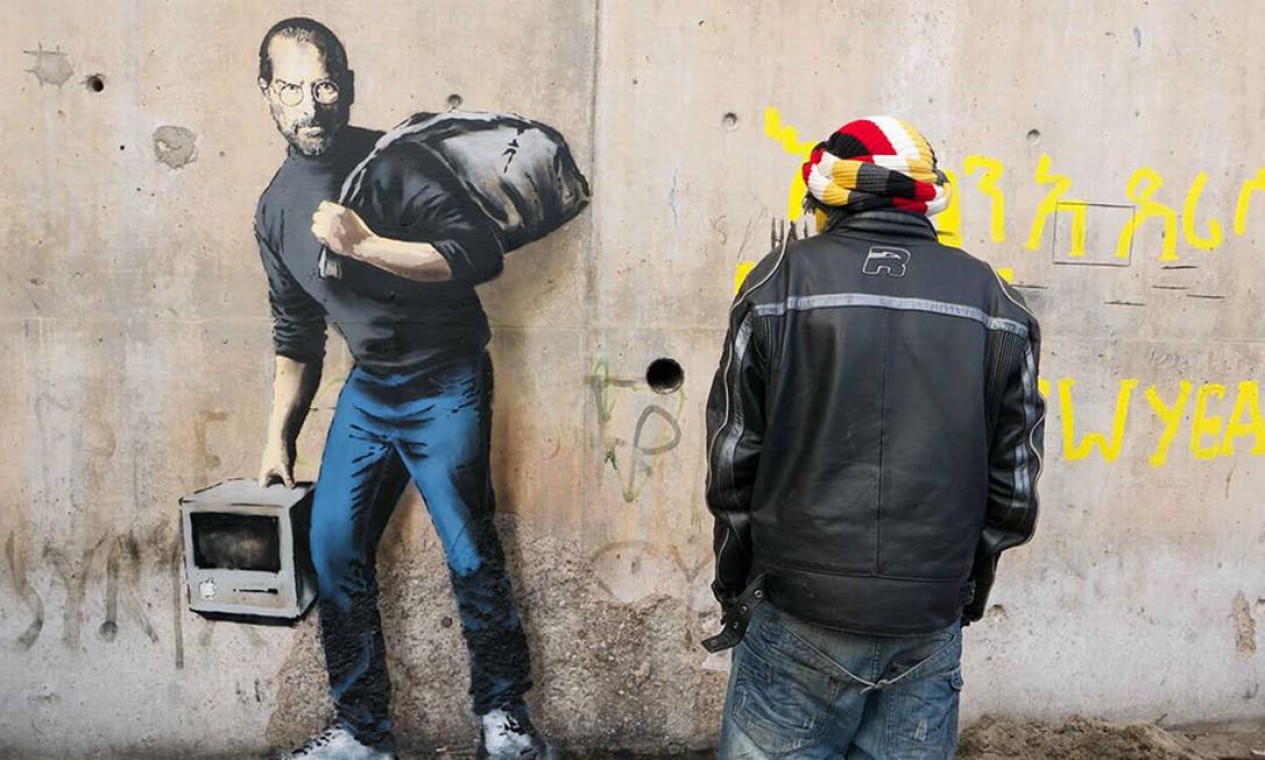 No grafite 'Filho de um imigrante da Síria', localizado em Calais, onde está situado um campo de refugiados, o artista lembra que o gênio Steve Jobs é filho de um imigrante Foto: Banksy / Reprodução