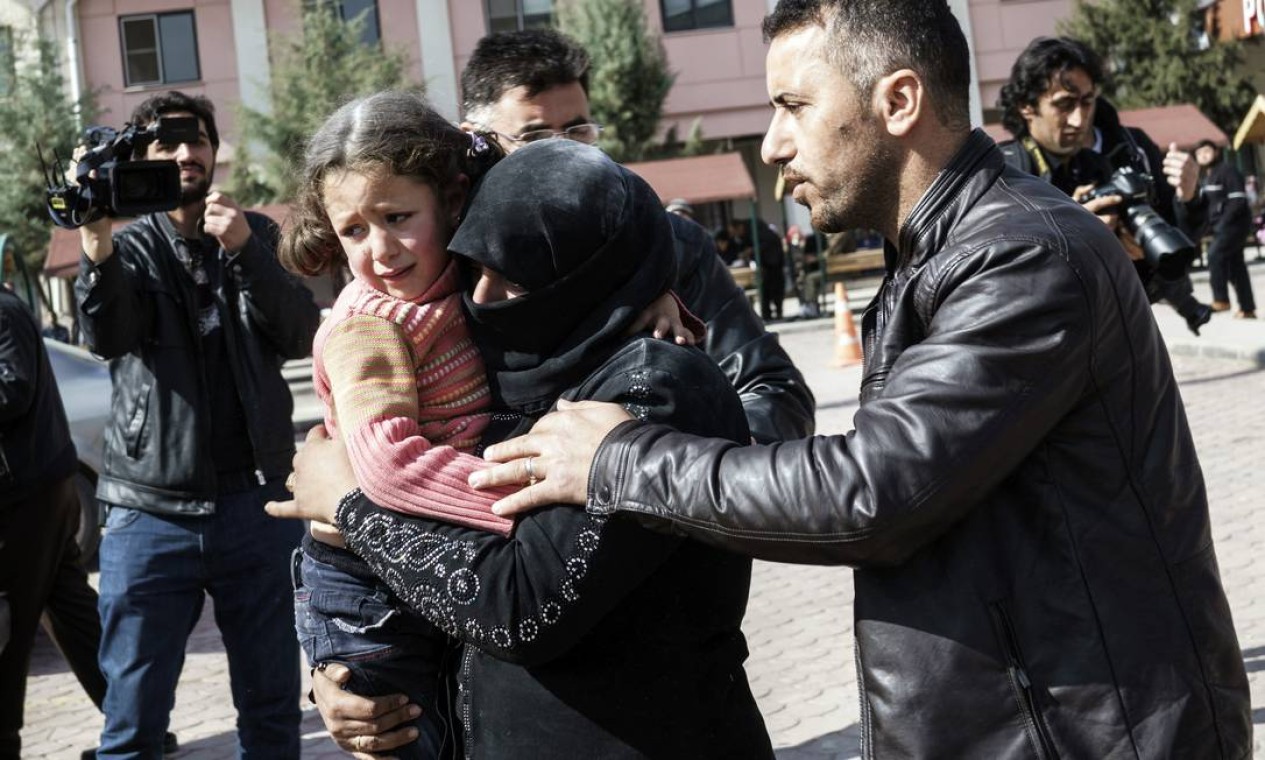 Homem turco ajuda mulher síria que carrega menina ferida ao hospital de Kilis, na Turquia Foto: Halit Onur Sandal / AP