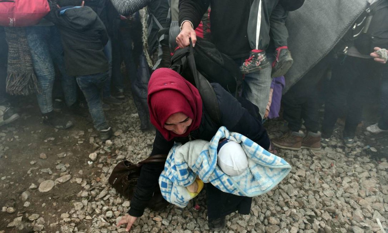 Mulher tenta proteger bebê durante tumultos na fronteira da Grécia, que tiveram gás lacrimogênio lançado pela polícia contra a multidão de imigrantes. Foto: LOUISA GOULIAMAKI / AFP