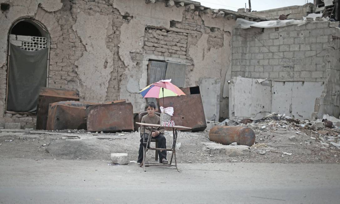 Na zona rural de Damasco, menino deslocado tenta vender alguns bens em frente a prédio danificado, enquanto cerca de 80% da população infantil síria sofre com a guerra Foto: UNICEF
