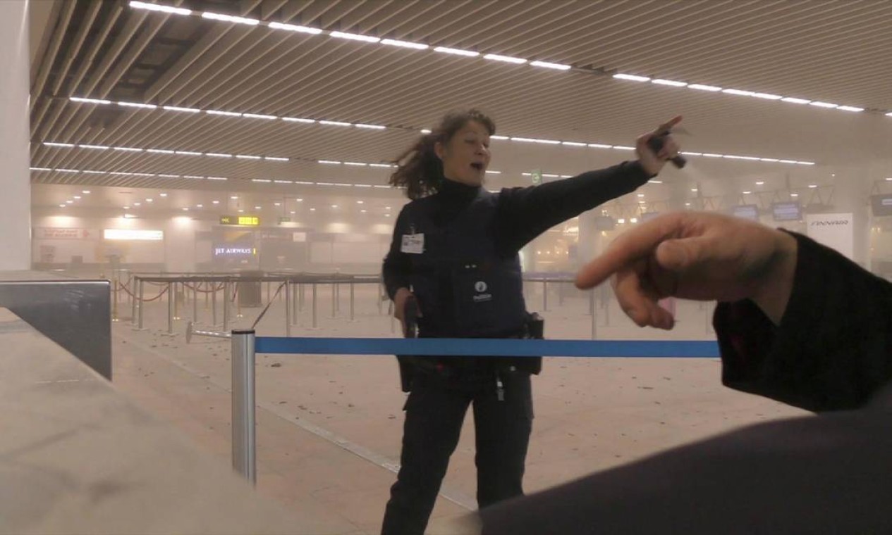 Foto de um passageiro mostra policial auxiliando os viajentes no terminal do aeroporto de Bruxelas tomado por fumaça, logo após os atentados na capital belga Foto: Ralph Usbeck / AP