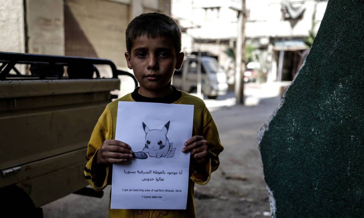 Menino segura um cartaz em foto divulgada pelas Forças Revolucionárias da Síria, com a imagem de um Pokemon e a frase: "Eu estou em Ghouta Oriental na Síria, venha me pegar!" Foto: HANDOUT / REUTERS