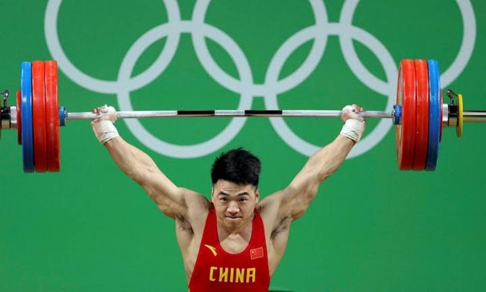 O atleta chinês estabeleceu o novo recorde mundial de arremesso na categoria até 85 quilos. Na modalidade, o atleta sustenta a barra com as anilhas em duas fases: primeiro, tira a carga do chão e, depois, precisa levantá-la sobre a cabeça, o que fez com 217 quilos. Foto: Divulgação / COI