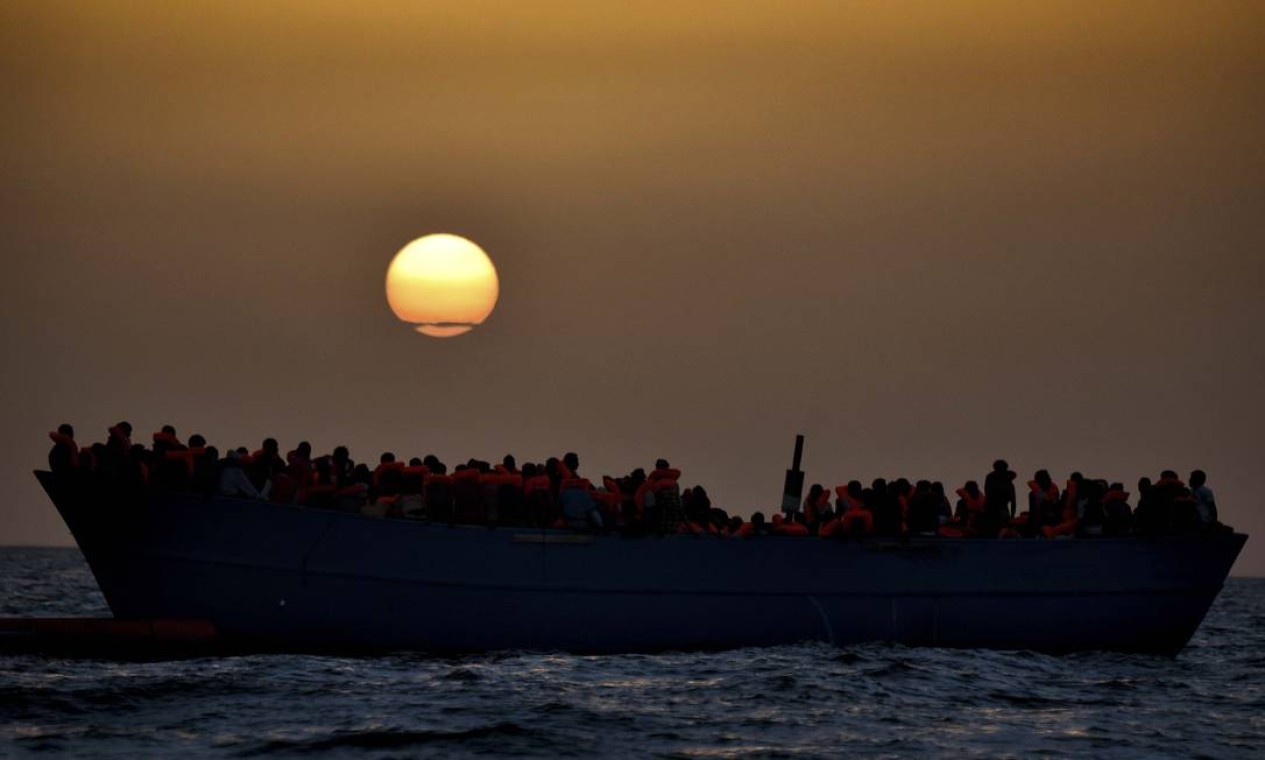 Grupo de imigrantes aguarda resgate no Mar Mediterrâneo, a 20 milhas náuticas da costa da Líbia, enquanto o sol se põe. Segundo relatório da Organização Internacional para as Migrações (OIM), 426 pessoas morreram no mar este ano tentando chegar à Europa Foto: ARIS MESSINIS / AFP