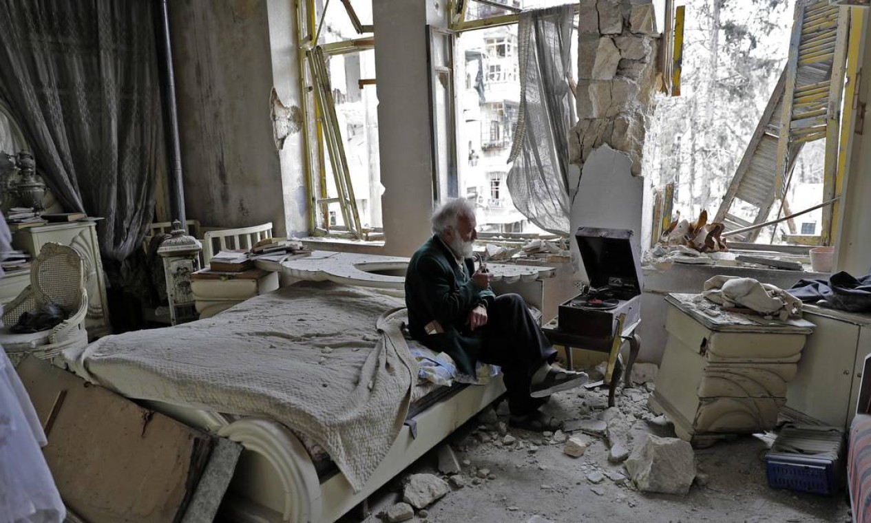 Mohammad Mohiedine Anis, de 70 anos, escuta música em quarto destruído na região de al-Shaar, área de Aleppo outrora controlada por rebeldes Foto: JOSEPH EID / AFP