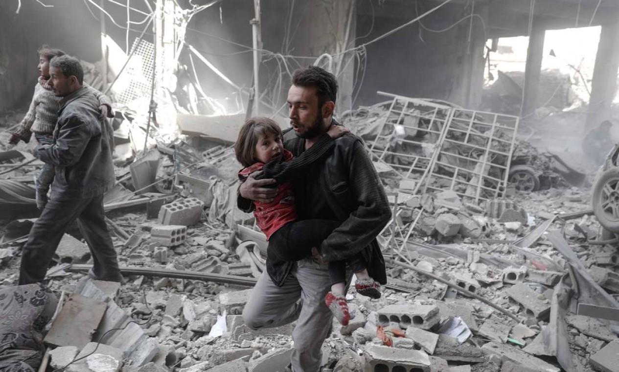 Homens carregam crianças pequenas após ataque aéreo em Douma; segundo a ONG Save The Children, a Síria vive uma crise de saúde mental infantil, uma vez que muitas crianças ficam traumatizadas pela violência da guerra Foto: SAMEER AL-DOUMY / AFP