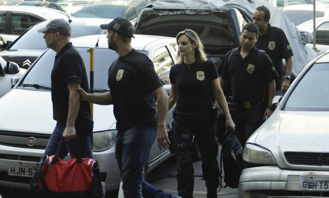 À frente dos policiais — e usando os mesmos trajes —, Côrtes é segurado pelo braço por um PF, enquanto carrega uma bolsa vermelha Foto: Gabriel de Paiva / O Globo