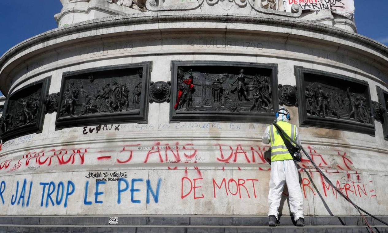 Um homem limpa a pixação em foi escrito "Macron ou Le Pen: 5 anos na rua" na estátua na praça da República, em Paris, um dia após o primeiro turno das eleições. Policiais e manifestantes contra Macron e Le Pen entraram em confronto neste domingo na região da Praça da Bastilha Foto: FRANCOIS GUILLOT / AFP
