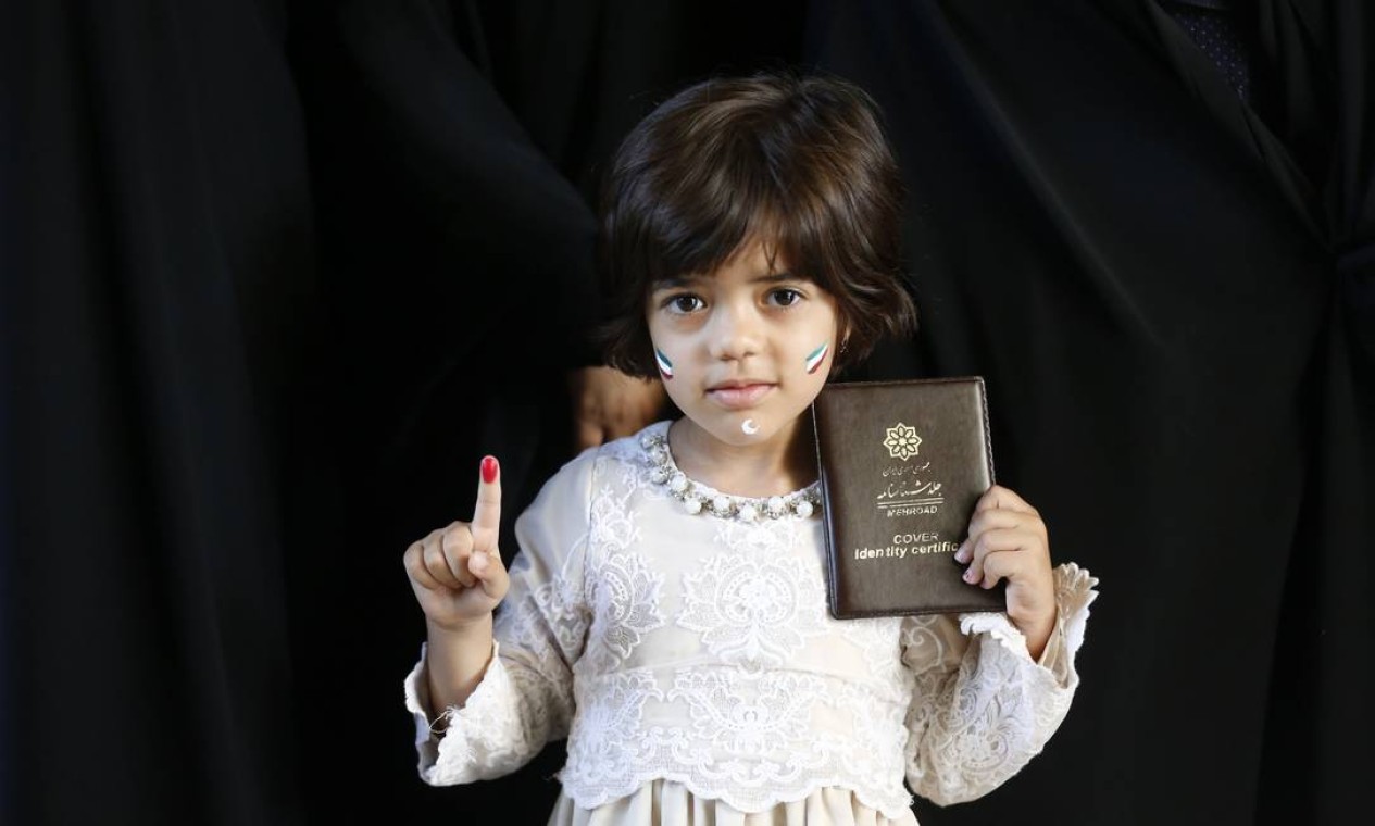 Uma menina iraniana mostra seu dedo pintado e a identidade de sua mãe depois de ter votado nas eleições presidenciais em um sessão eleitoral em Teerã Foto: ATTA KENARE / AFP