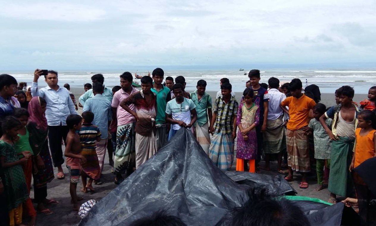 Pessoas assistem enquanto um homem cobre os corpos de mulheres e crianças rohingya que morreram afogados, após os barcos em que estavam naufragarem no rio Naf Foto: SUZAUDDIN RUBEL / AFP