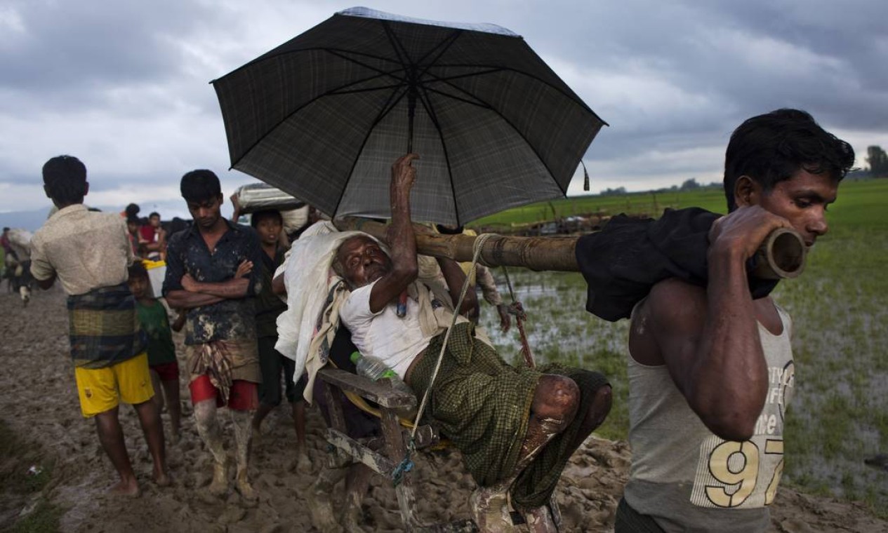 Homem idoso é carregado nos ombros para atravesar campos de arroz; rohingyas são perseguidos e, não raro, mortos em Mianmar Foto: Bernat Armangue / AP