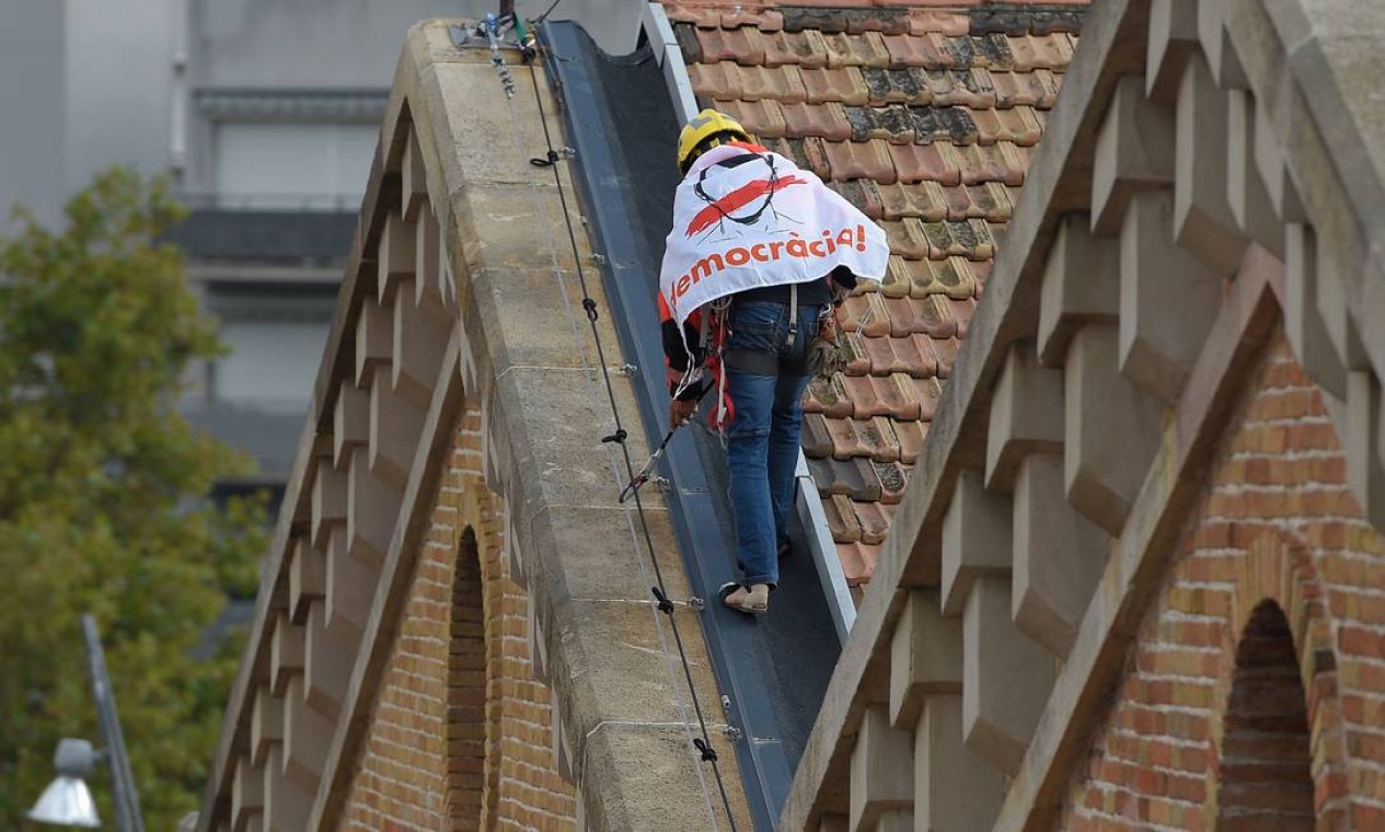 Bombeiro trabalha com faixa que diz "Democracia" em telhado perto do Museu de História da Catalunha em Barcelona Foto: LLUIS GENE / AFP