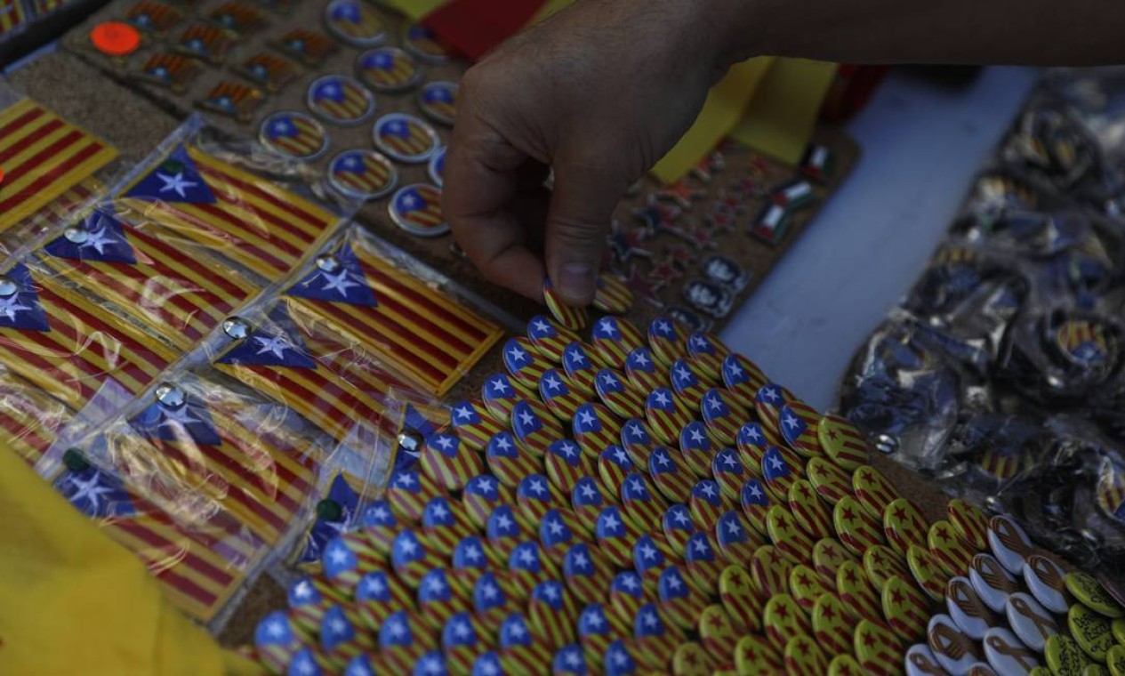 Um homem pendura botons que com a bandeira da Catalunha, imagem que simboliza e reforça a independência local Foto: Santi Palacios / AP
