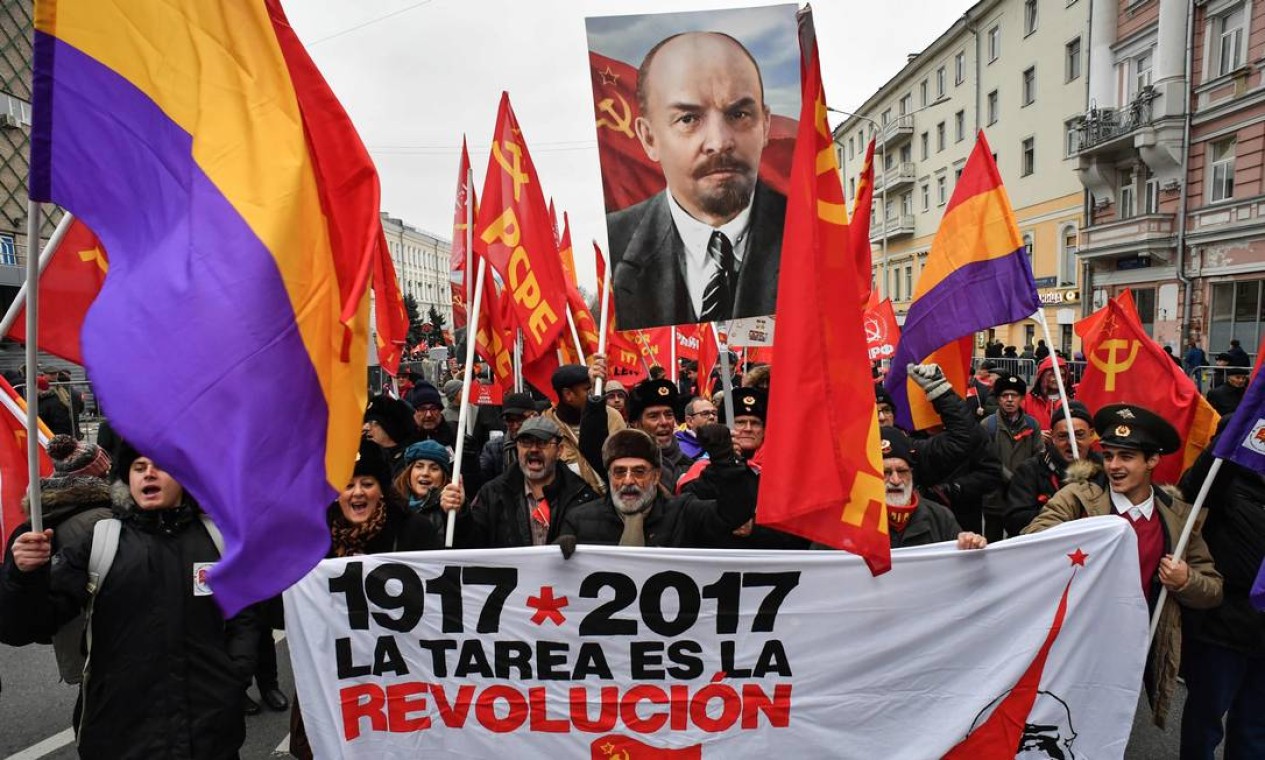 Russos levam pôster que diz que "A tarefa é a revolução" junto com foto de Vladimir Lenin em marcha no centro de Moscou. O aniversário da Revolução Russa foi celebrado com suntuosidade no período soviético, com um grande desfile no Praça Vermelha a cada 7 de novembro Foto: YURI KADOBNOV / AFP