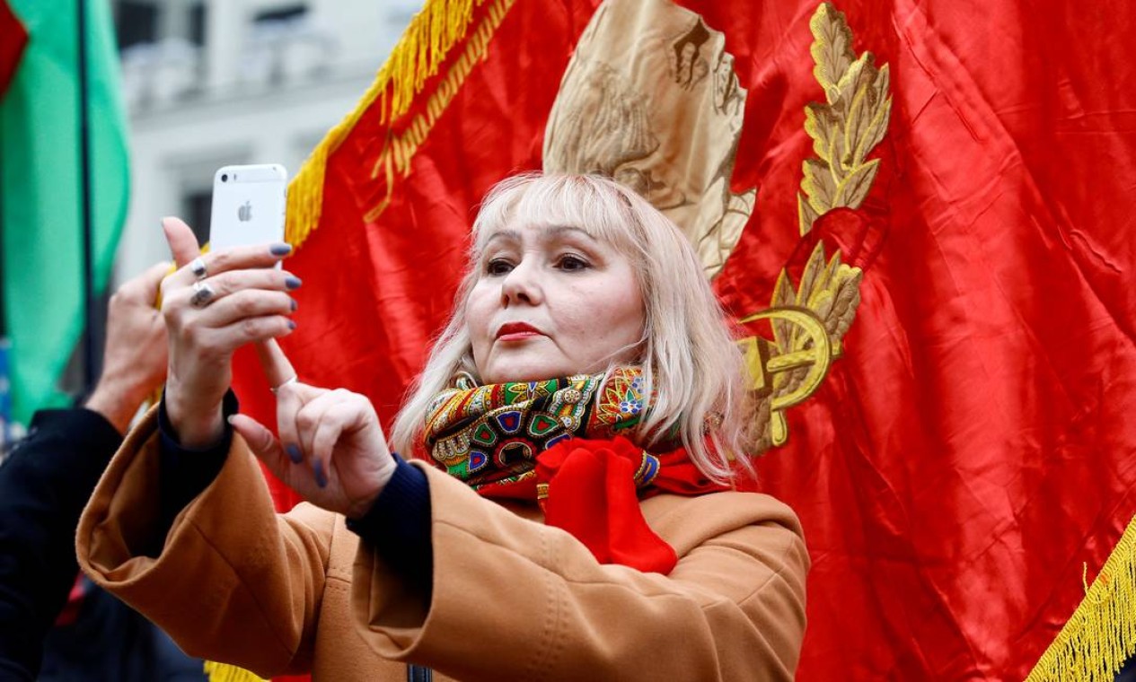Mulher faz selfie com imagem de Vladimir Lenin sobre bandeira em Minsk. Até o momento, o presidente russo, Vladimir Putin, evitou participar da maior parte dos eventos organizados para celebrar o centenário Foto: VASILY FEDOSENKO / REUTERS