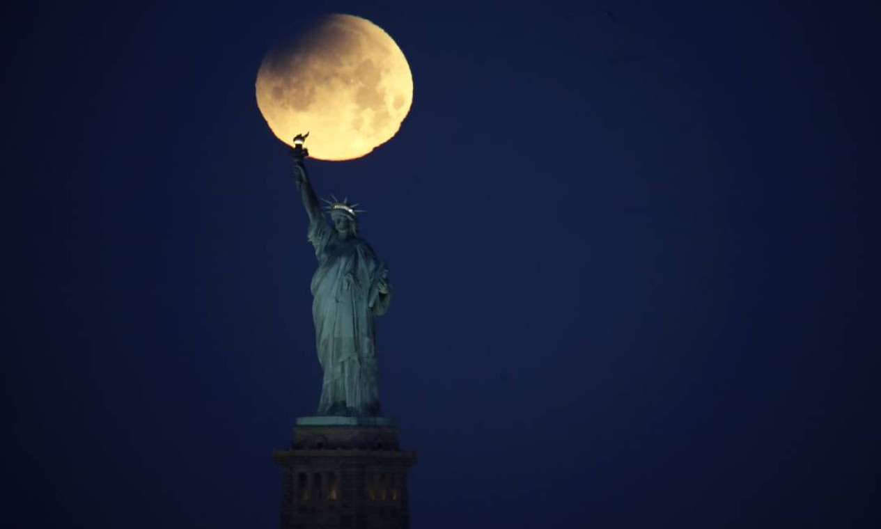A Lua cheia parcialmente coberta acima da Estátua da Liberdade, em Nova York Foto: Julio Cortez / AP