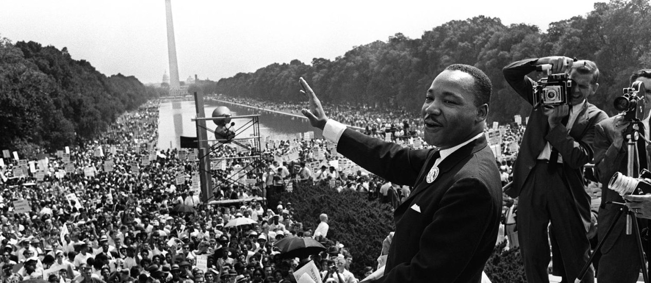 Em 1963, Martin Luther King, líder do movimento pelos direitos civis nos EUA, acena para multidão em durante a Marcha em Washington; o ativista liderara o boicote aos ônibus após o caso Rosa Parks e, a partir de então, foi ganhando protagonismo na luta dos negros. Neste dia, ele fez o seu mais famoso discurso, intitulado "Eu tenho um sonho" Foto: AFP