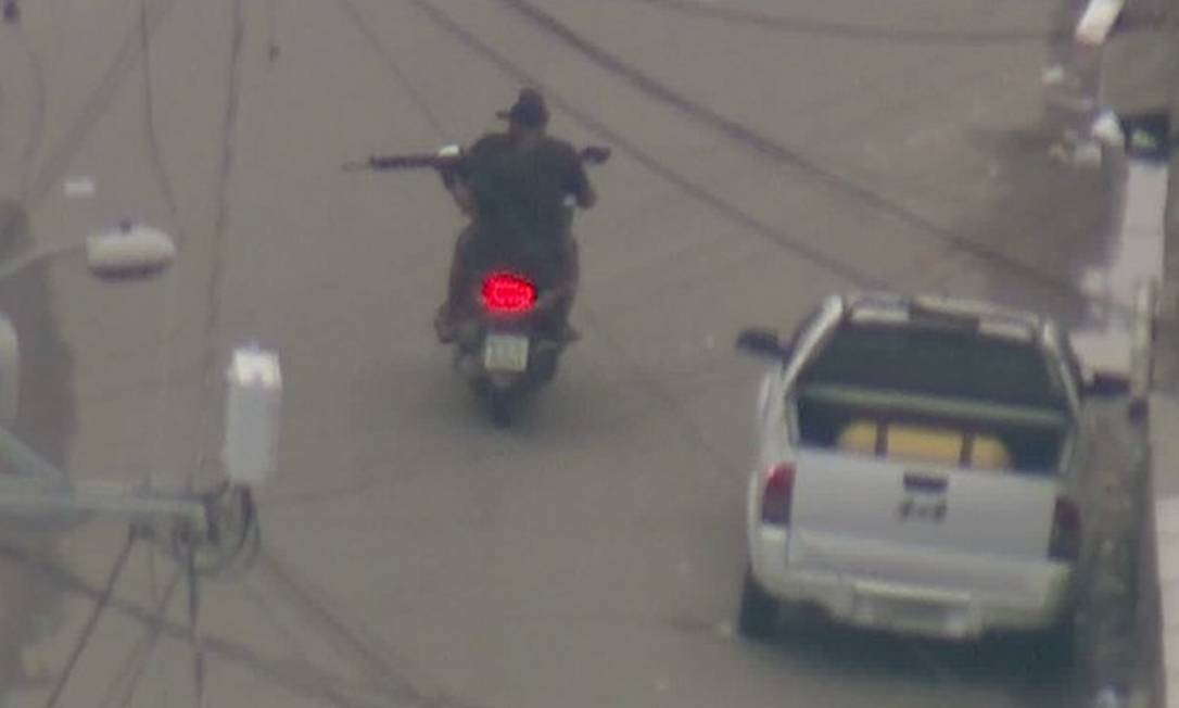 Homem armado com fuzil circula em moto por rua da Cidade de Deus Foto: Reprodução / Bom Dia Rio